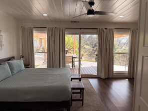 Un dormitorio con cama, ventilador de techo y vistas al exterior a través de amplias ventanas.