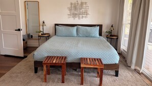 A bedroom with a bed, two wooden stools, a mirror, a wall art piece, and a window with curtains. - Good Vibes getaway lake views, Marina, private Boat Slip (Bass Lake)