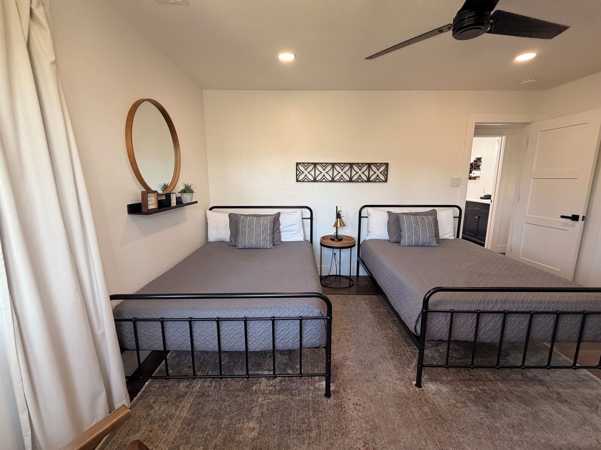 A bedroom with two beds, a ceiling fan, a small table, and a door leading to a bathroom.