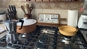 A kitchen with a stove, a pot, a coffee maker, and a sign on the wall. - Serenity Inn (Quito)