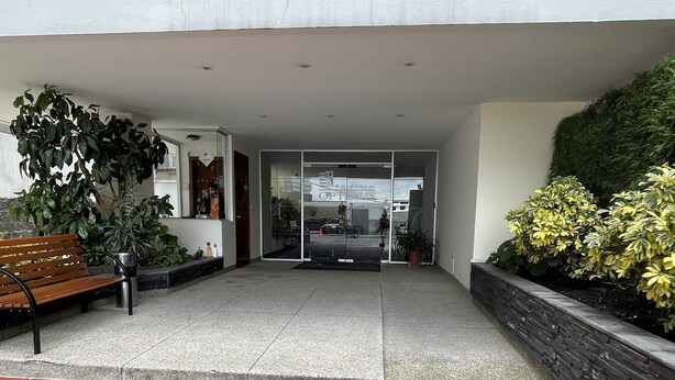 A modern building entrance with a tiled patio, a bench, and potted plants. - Serenity Inn (Quito)