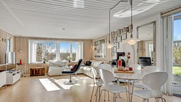 Una sala de estar moderna con sofá, sillas, una mesa de comedor y ventanas grandes.