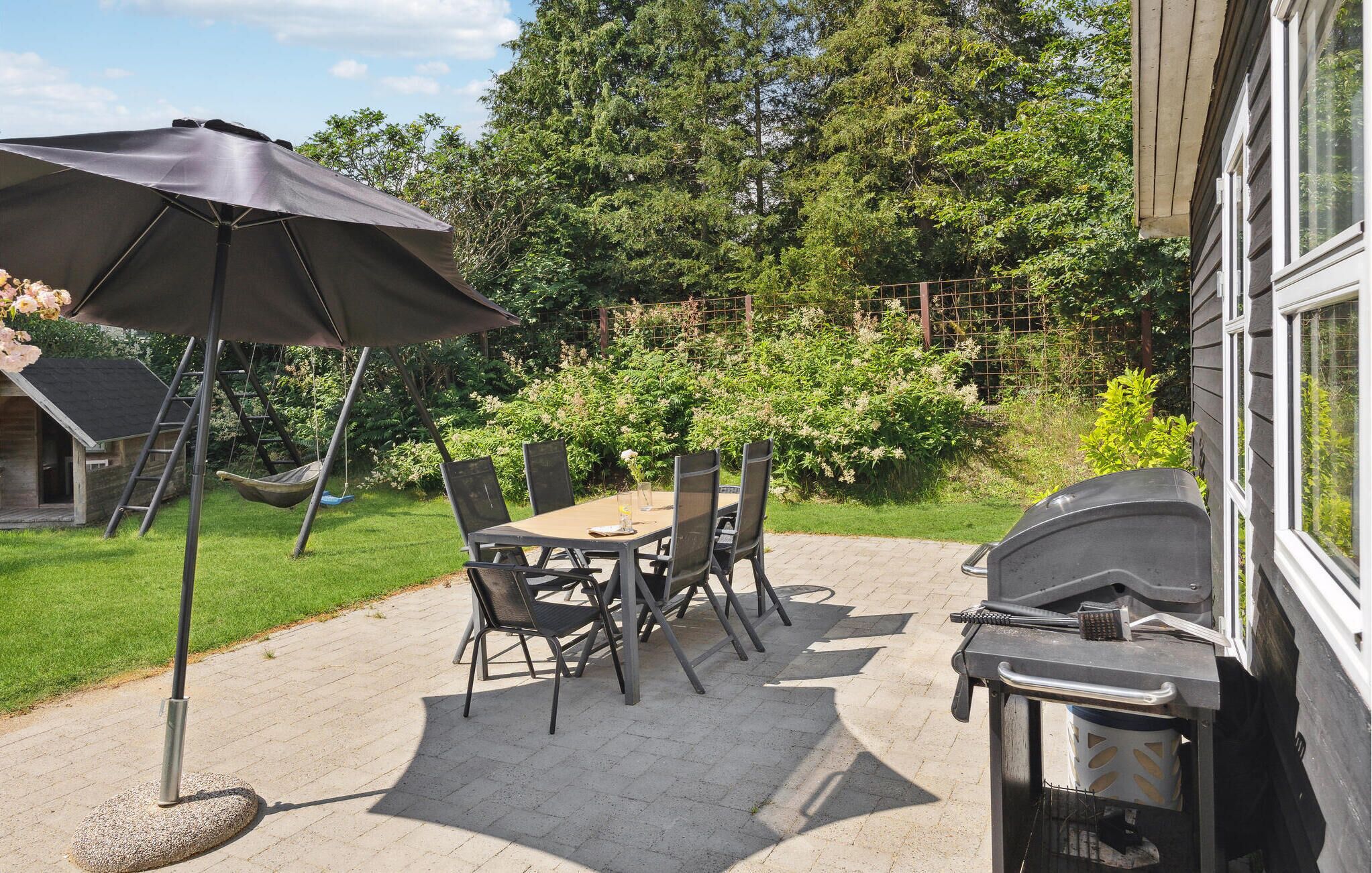 Un patio al aire libre con una mesa, sillas, una parrilla y un conjunto de columpios.