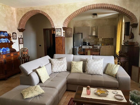 A living room with a sectional sofa, a coffee table, and a kitchen in the background.