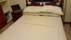 A bed with white bedding and a laptop on a wooden nightstand.