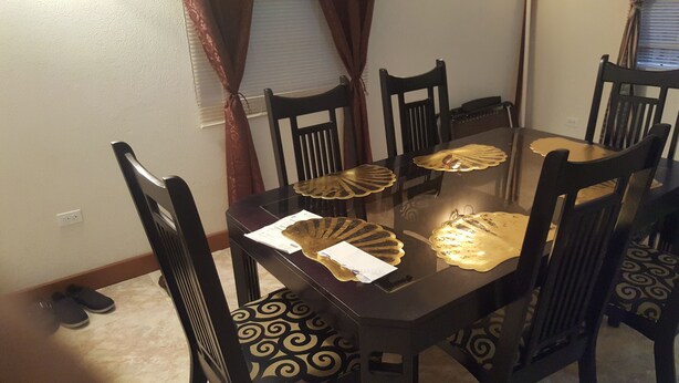 A dining table with four chairs, a pair of slippers, and a window with curtains.