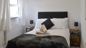 A neatly made bed with a black and white duvet, two bedside lamps, and a window with white curtains. - Old Colliery Cottage (Shilbottle, near Alnwick)