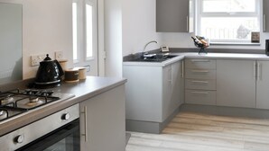 A modern kitchen with a gas stove, oven, and a window with a view. - Old Colliery Cottage (Shilbottle, near Alnwick)