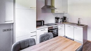 A compact kitchen with white cabinets, a microwave, stove, and a sink. There are two chairs and a wooden table.