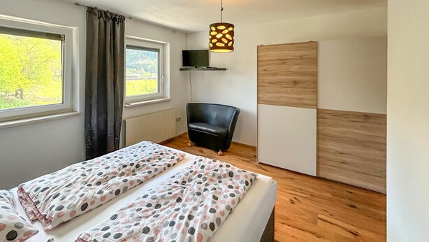 A bedroom with two beds, a chair, a TV, and a window with curtains.