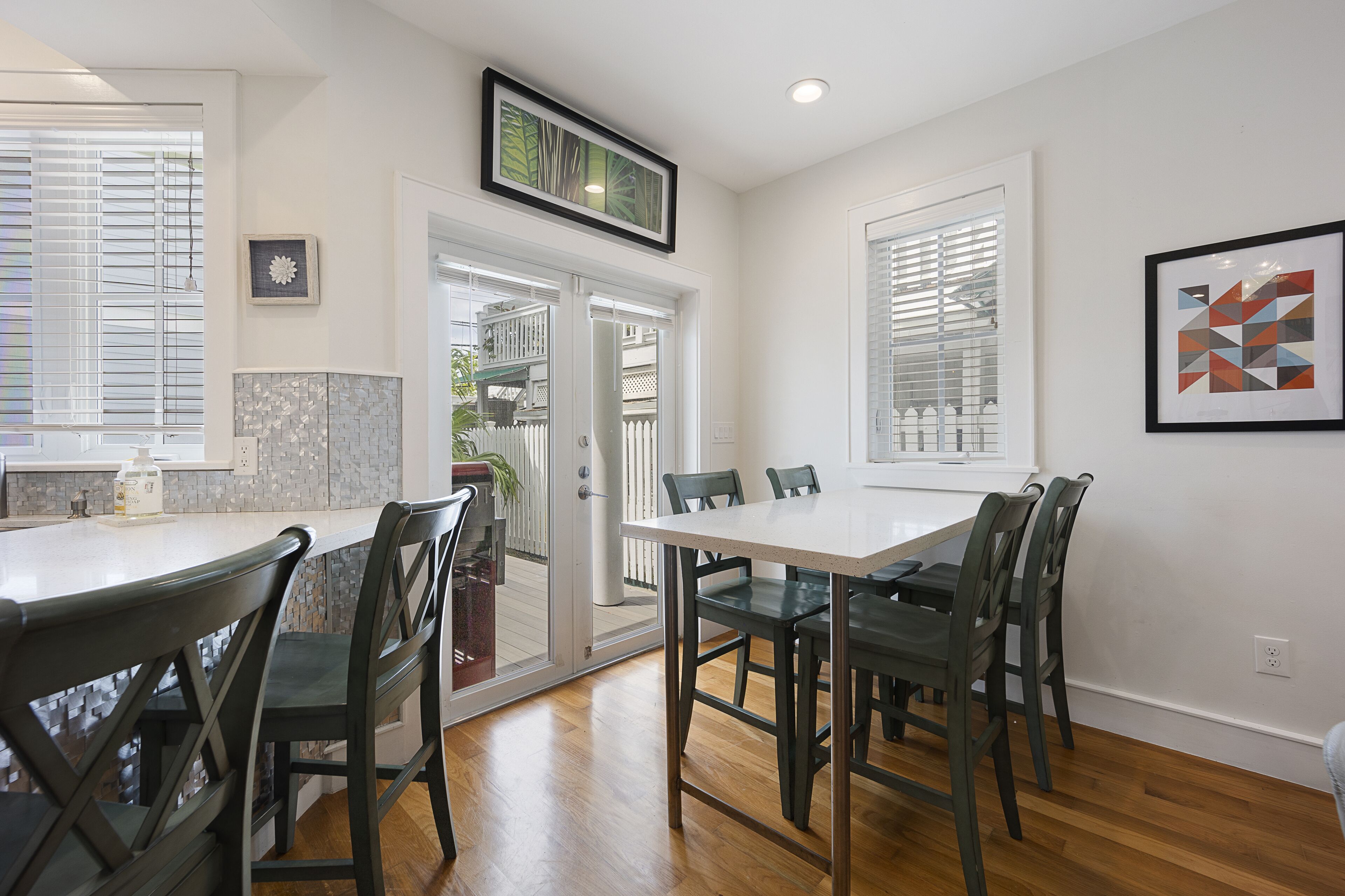 A dining area with a white table and dark chairs, a kitchen with white cabinets, and a door leading to a balcony.