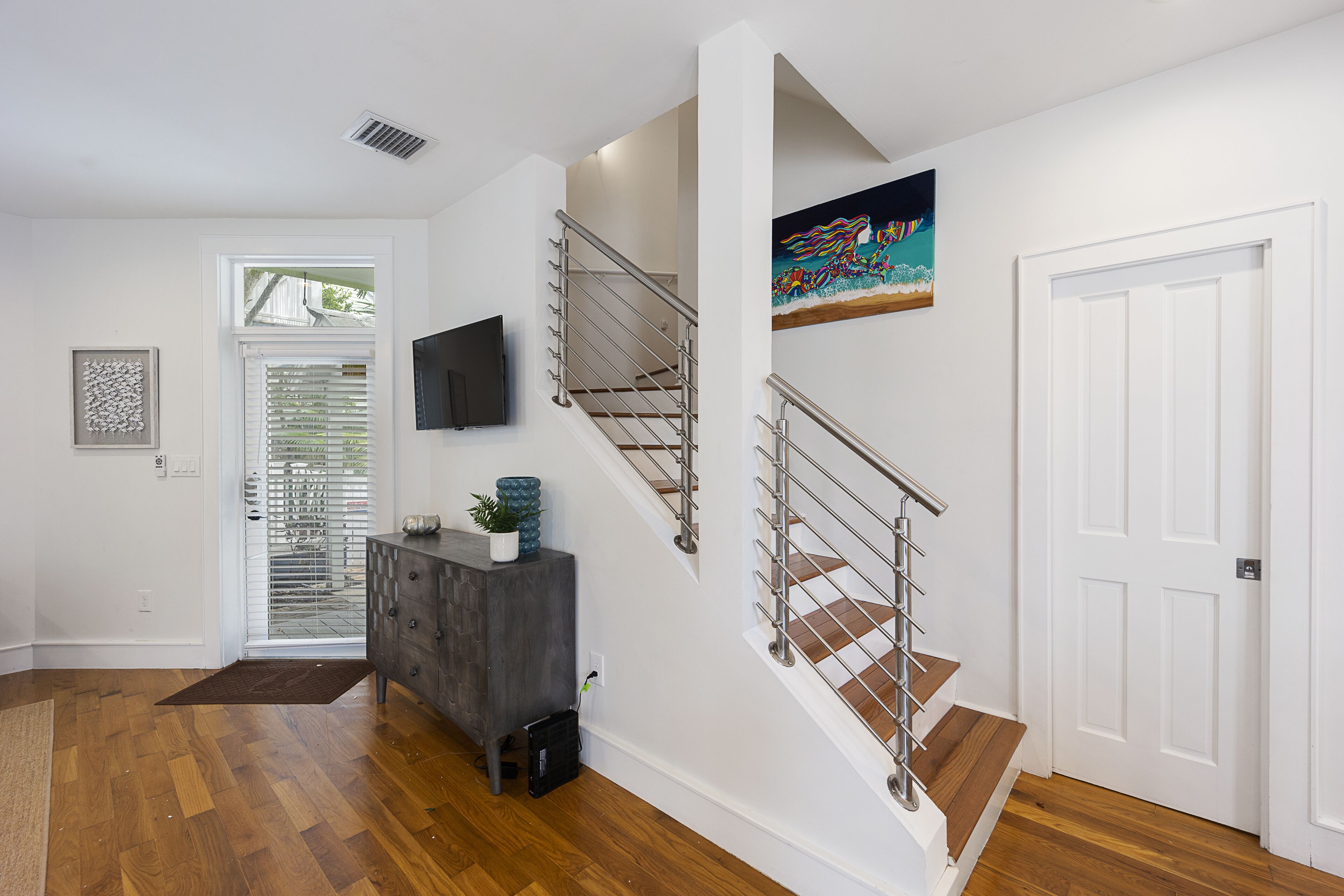 A staircase with metal railings, a flat-screen TV mounted on the wall, and a door with a white frame.