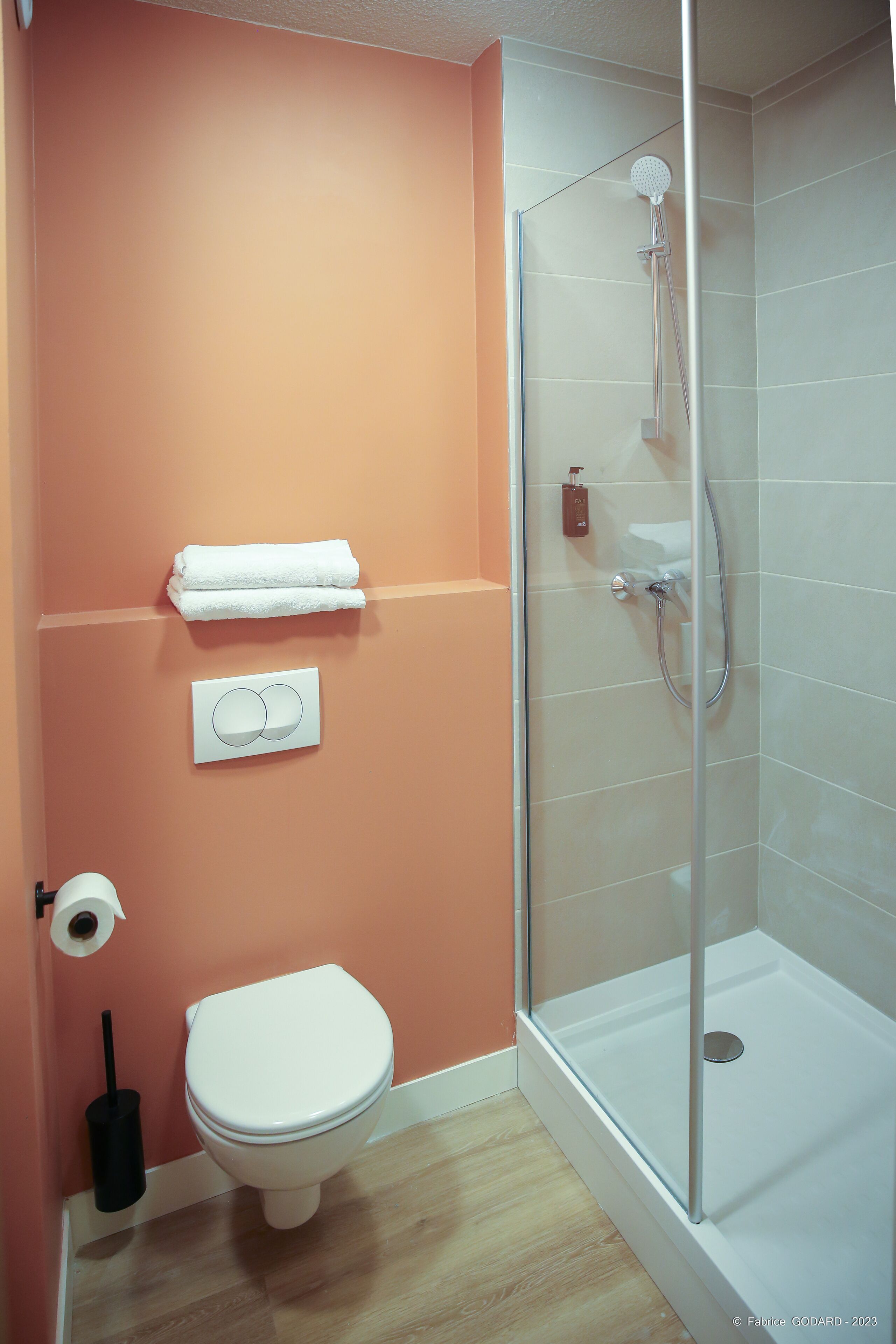 A bathroom with a toilet, a towel rack, a shower with a glass door, and a toilet paper holder.