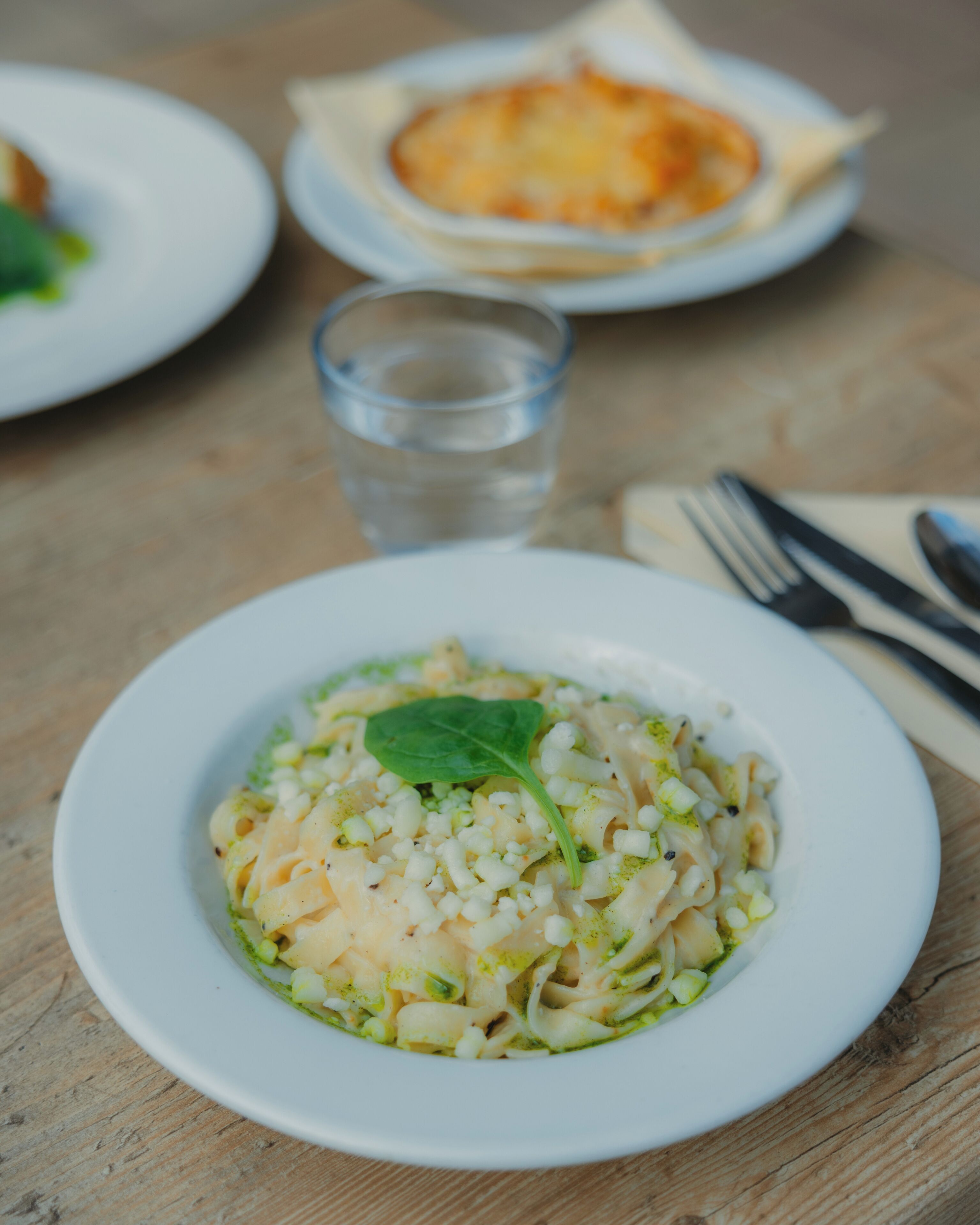 Une assiette de pâtes, garnie d’une feuille verte, posée sur une table en bois.