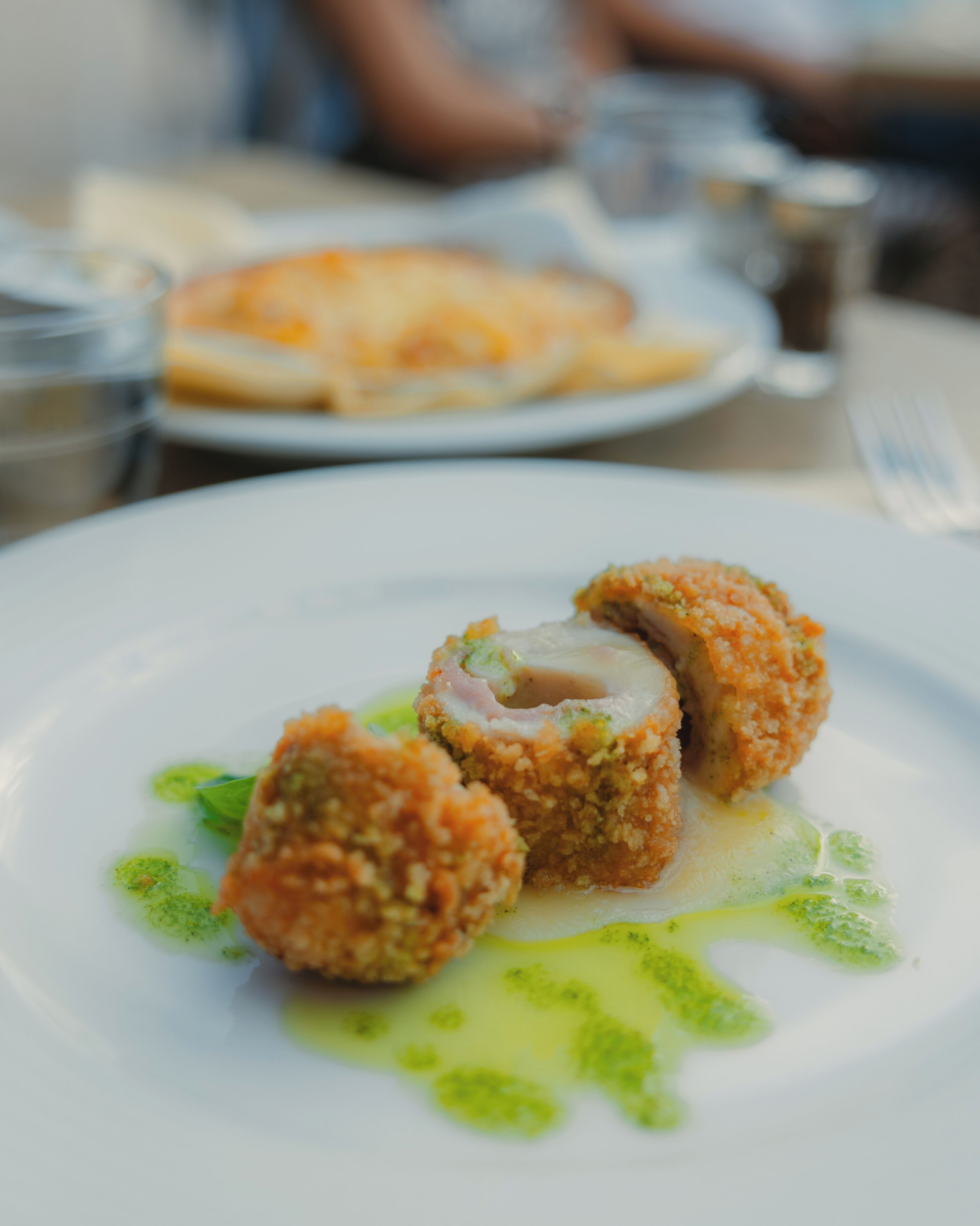 A plate with a food item, possibly a croquette, with a green sauce on a white plate.