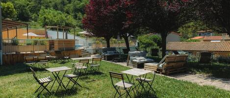 An outdoor seating area with tables and chairs, a wooden deck, and a tree with red flowers.