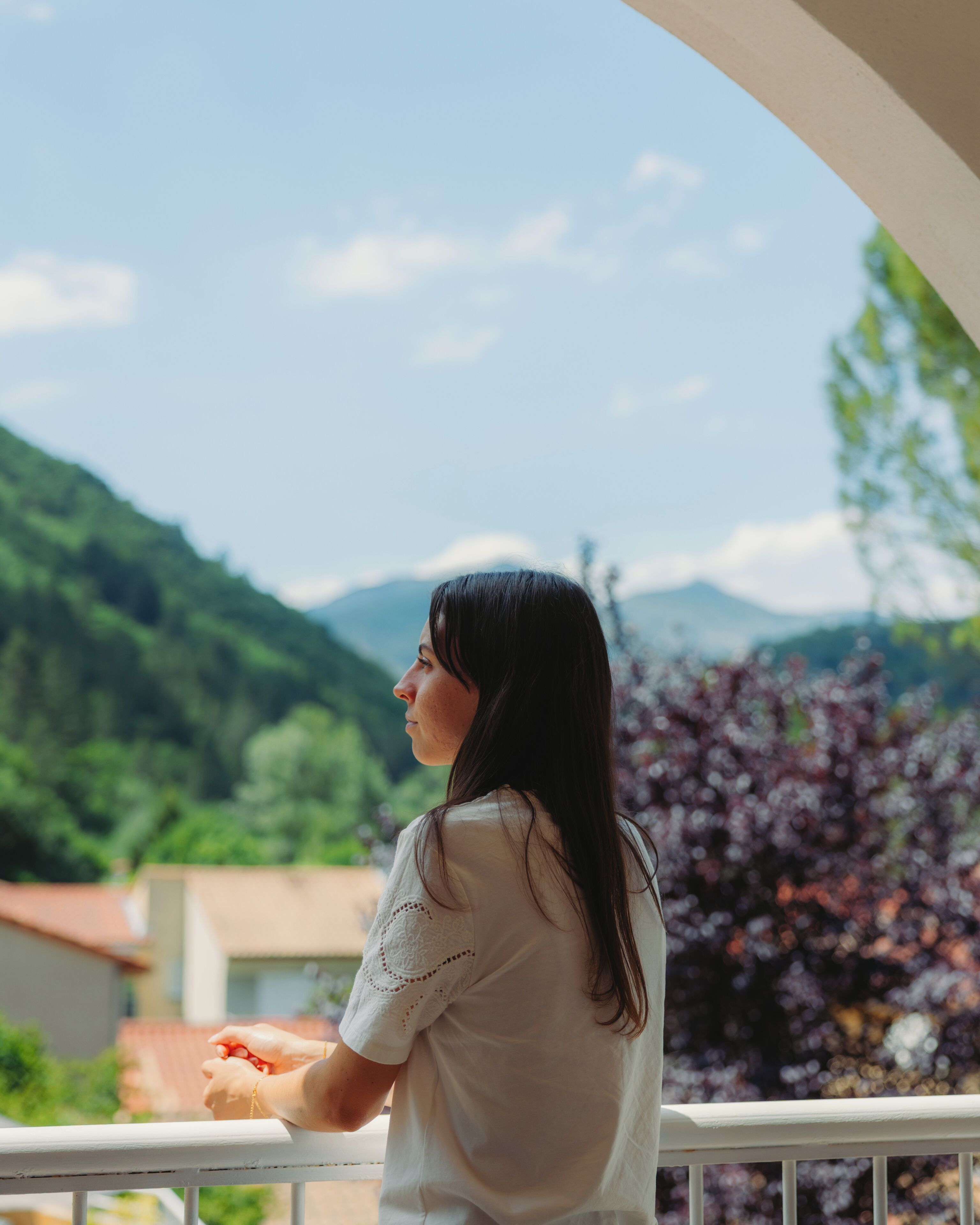 Una persona está de pie en un balcón con vista a un paisaje montañoso, con vegetación y cielo despejado.