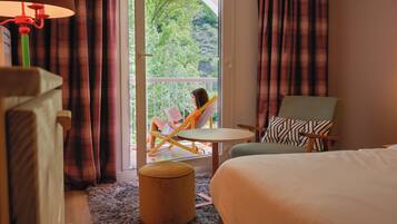 Habitación de hotel con cama, una silla, una mesita y vistas a zonas verdes.