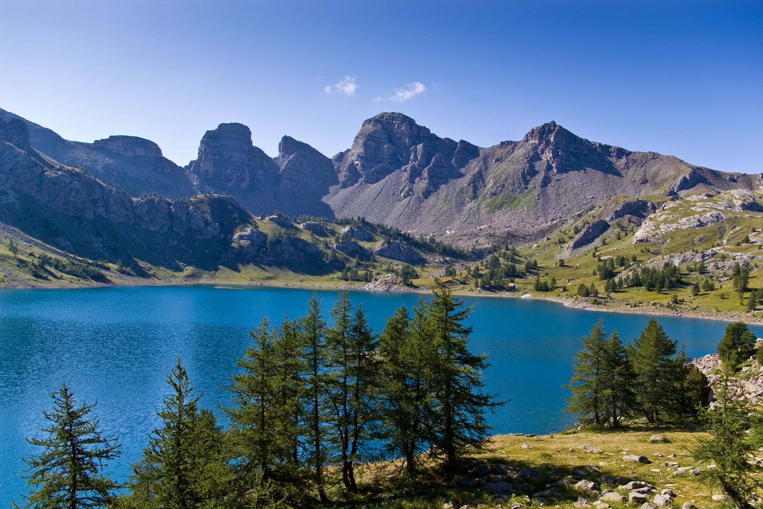 A mountainous landscape with a clear blue lake, surrounded by green trees and rocky terrain.