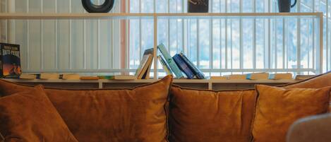A cozy living room with a sofa, a coffee table, and a bookshelf against a window with blinds.