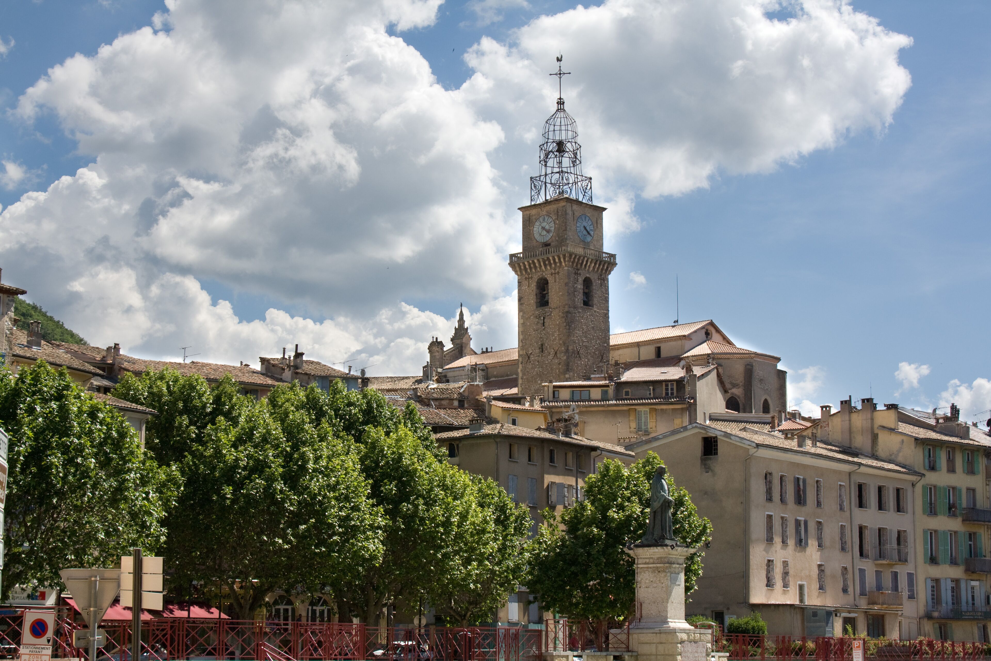 A historic town with a prominent clock tower, surrounded by traditional buildings and lush green trees.