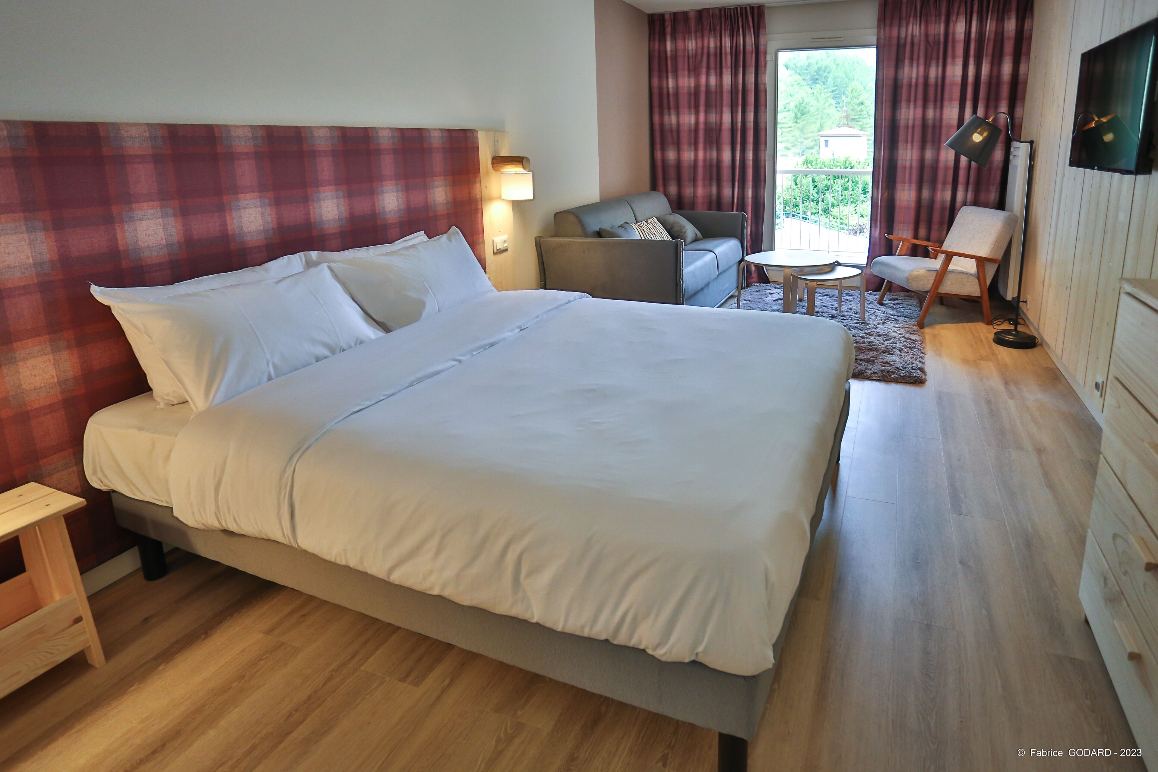 A hotel room with a large bed, a sofa, a small table, and a TV.