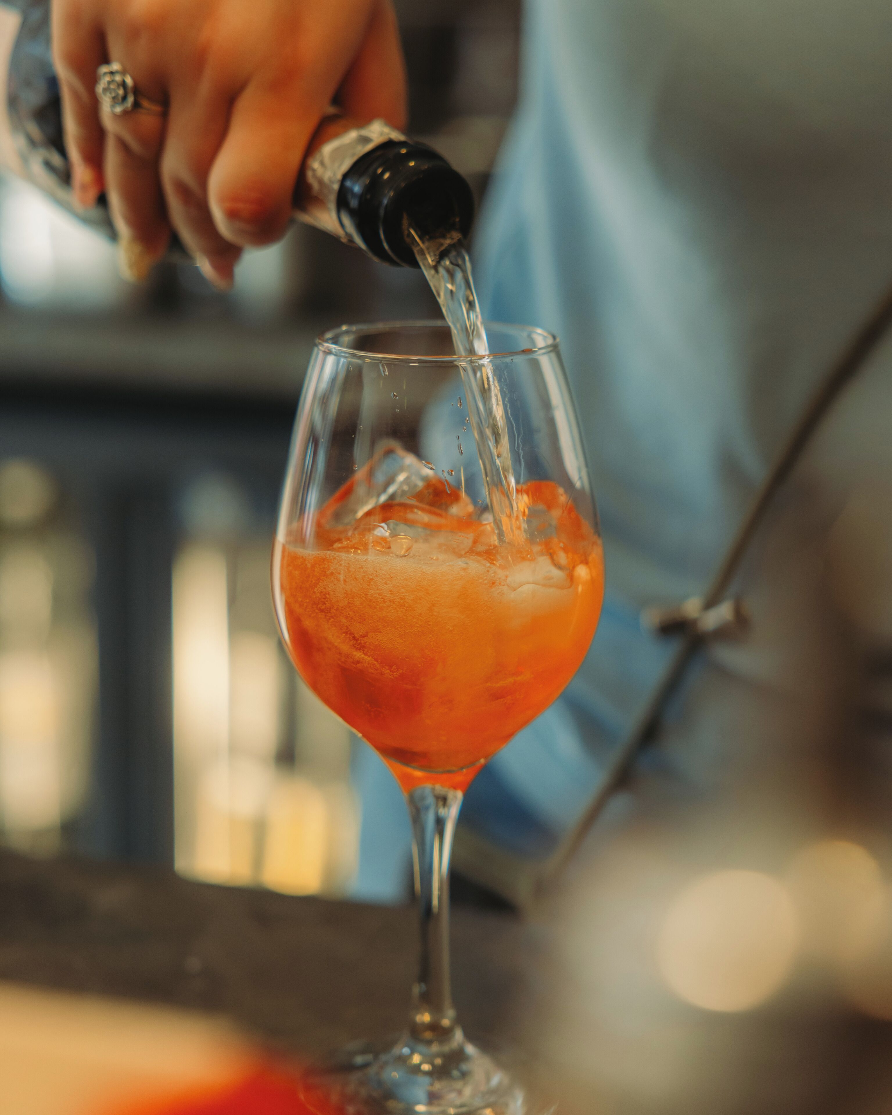 Une main verse un liquide transparent dans un verre rempli de glaçons.