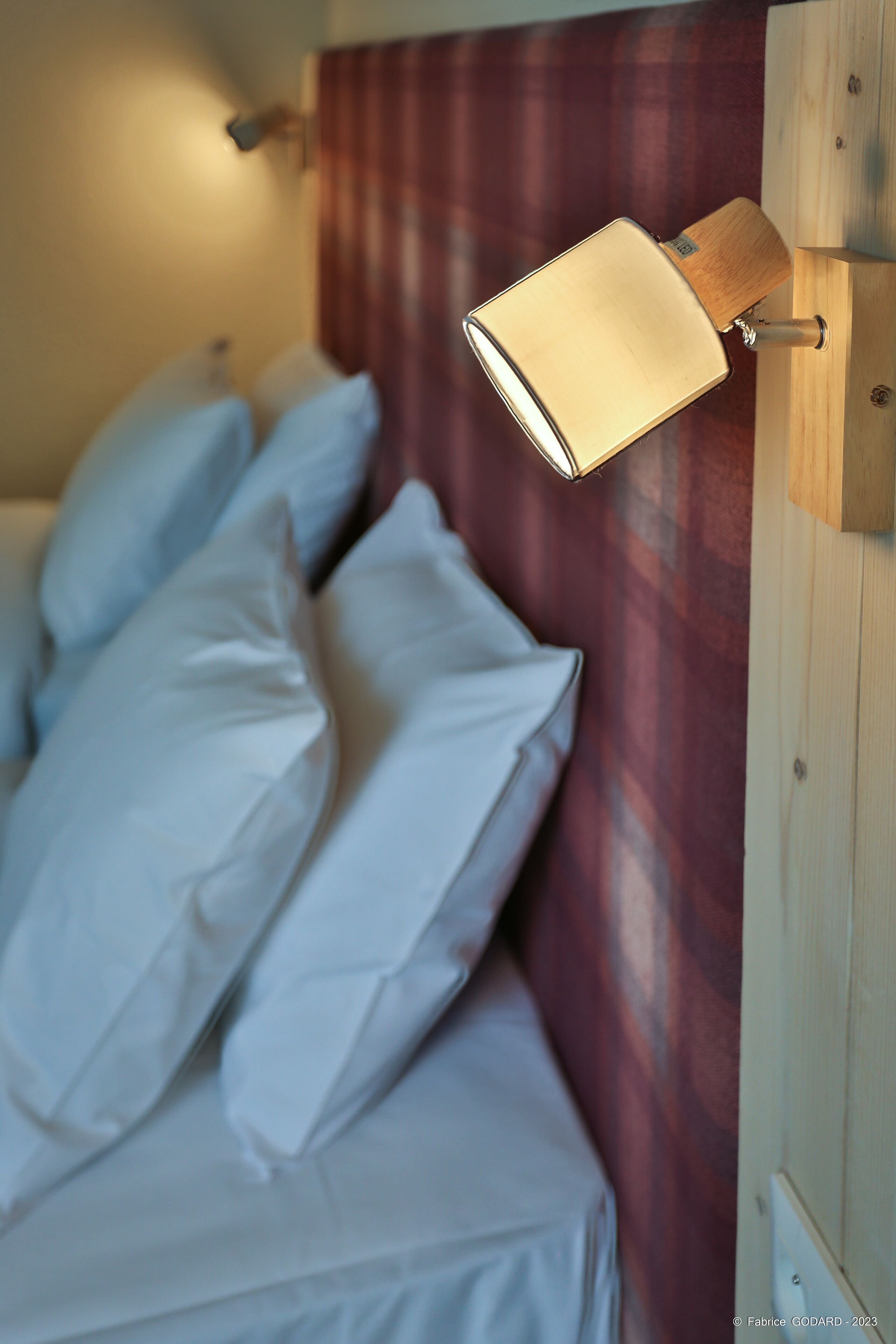 A bed with white linens and a wall-mounted lamp.