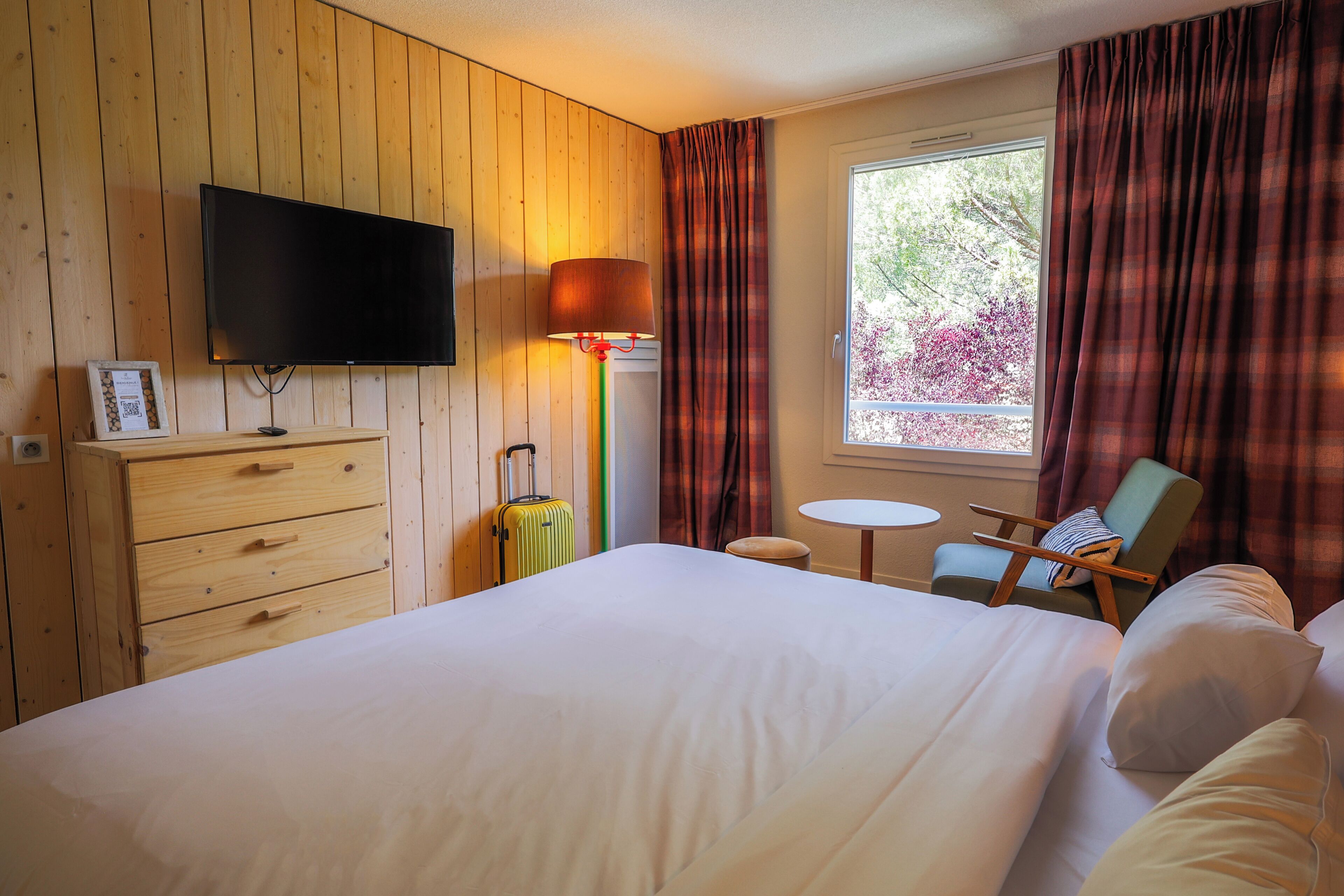 A hotel room with a bed, a television, a desk, a chair, and a window with curtains.