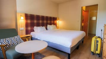 A hotel room with a bed, a small table, a chair, and a suitcase.