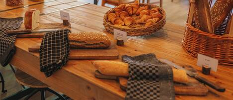 A wooden table with various baked goods, including bread and pastries, and a basket of croissants.