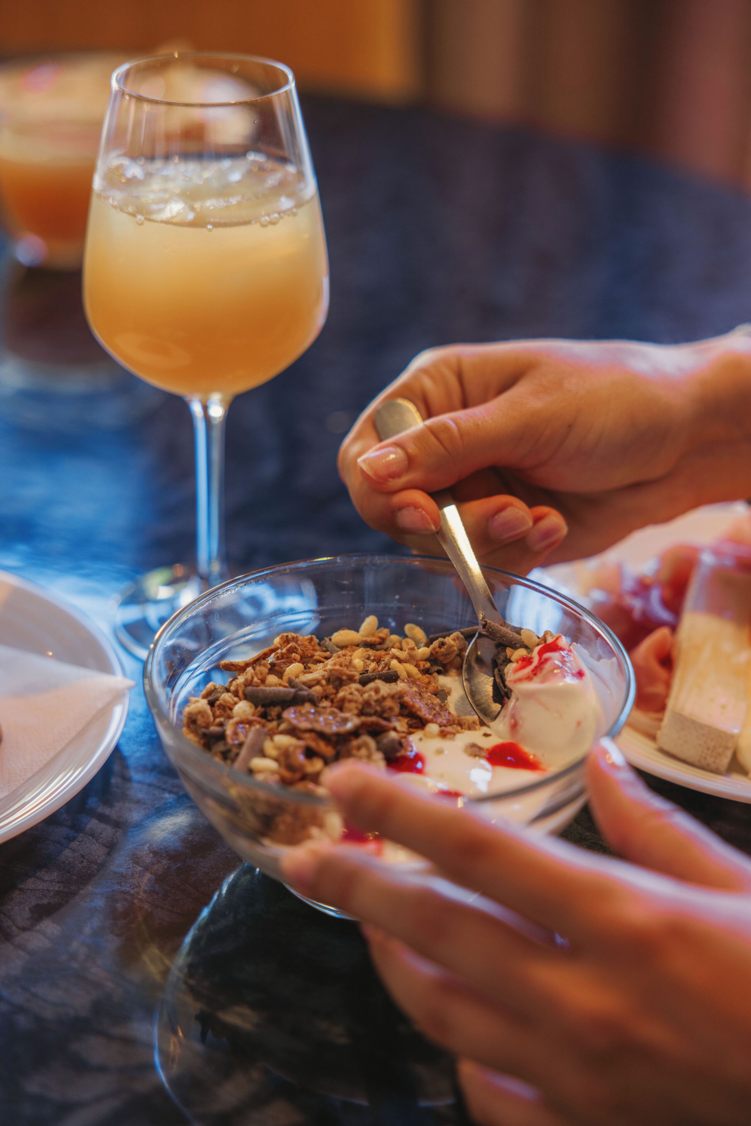 Una mesa de comedor con un vaso de bebida y un tazón de cereal con una cuchara.