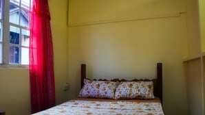 Un lit simple avec une literie à motifs floraux, une tête de lit en bois et une fenêtre ornée de rideaux rouges.