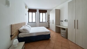 Un dormitorio con cama, dos ventanas, un escritorio y armarios empotrados.