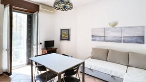 Una habitación con una mesa de comedor, sillas, un sofá, un televisor, un cuadro enmarcado y una lámpara de vitral.