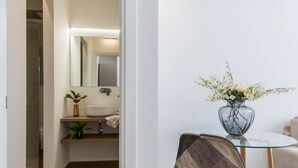 Un baño moderno con un espejo, un lavabo y un florero con flores sobre una mesa de vidrio.