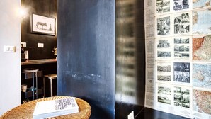 A room with a dark wall, a framed picture, a map, and a wicker table with a book. - Hosmate - Milano - Sammartini's Cave - Stazione Centrale (Milano)