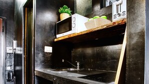 A kitchen with a microwave, sink, and wooden shelf with a plant and basket. - Hosmate - Milano - Sammartini's Cave - Stazione Centrale (Milano)