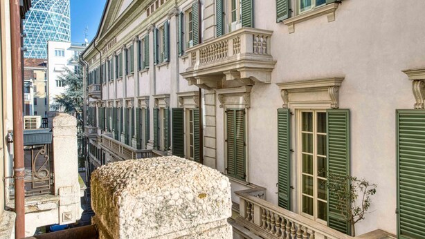 Una stretta via con edifici storici, una balaustra in pietra e un moderno edificio in vetro sullo sfondo.