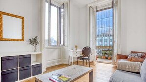 Un soggiorno moderno con un tavolino in legno, una poltrona, una scrivania e una sedia. Ampie finestre offrono vista sulla città.
