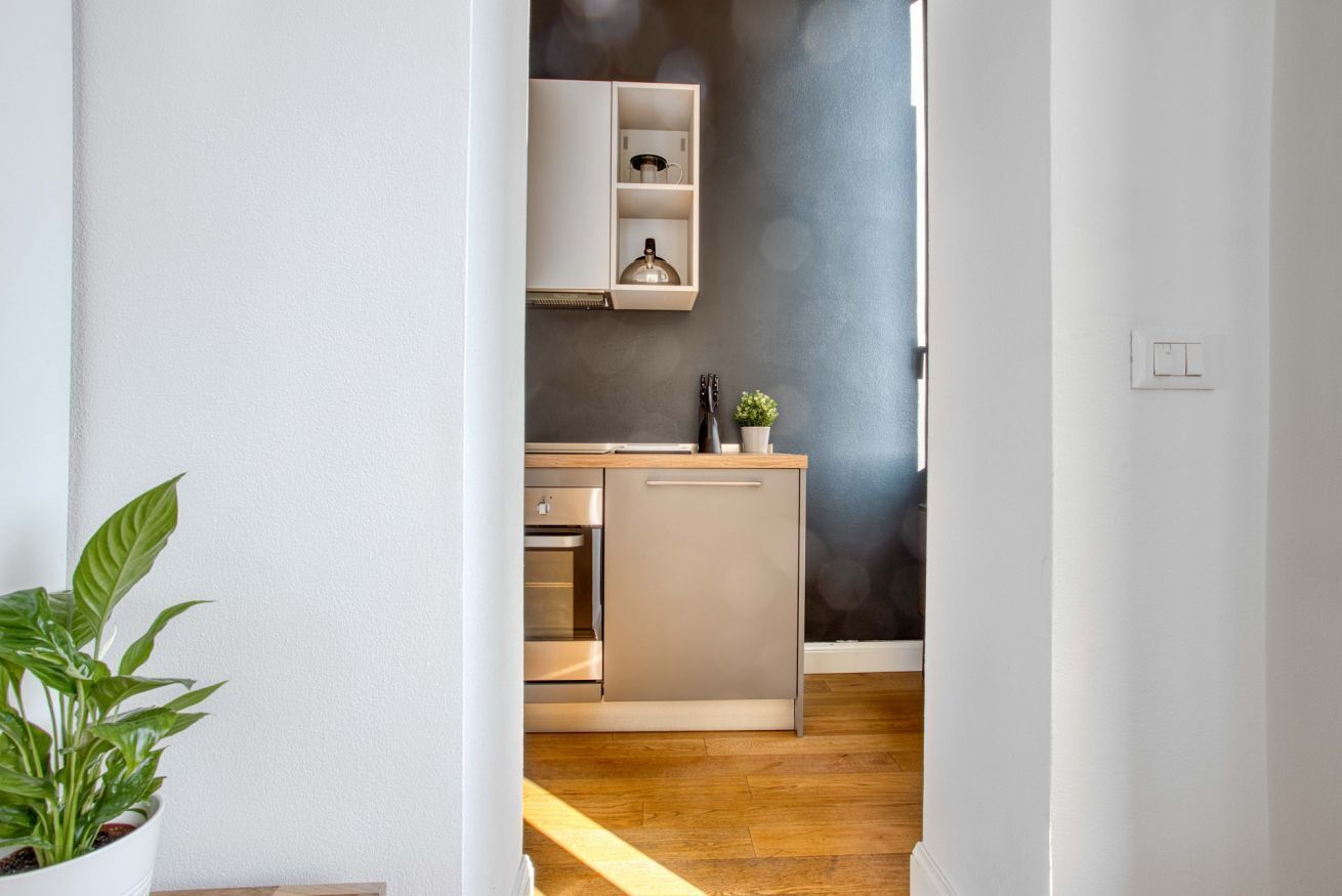 A narrow hallway leading to a kitchen with a built-in oven, a sink, and a cabinet above the counter.