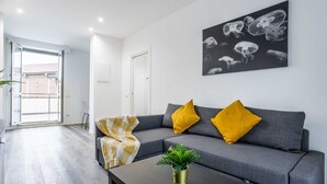 Een moderne woonkamer met een grijze bank, gele kussens, een zwarte salontafel en een wandkunst met kwal.
