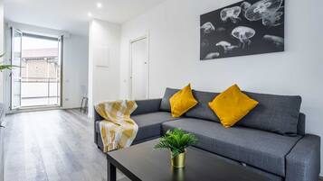 A modern living room with a grey sofa, yellow cushions, a black coffee table, and a wall-mounted artwork of jellyfish.