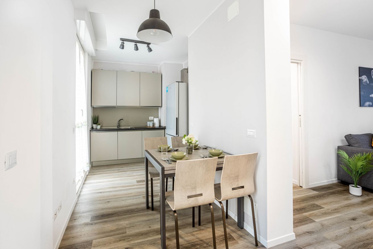 A modern kitchen with white cabinets, a dining table with chairs, and a pendant light.