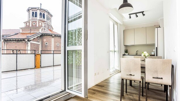 Een moderne keuken met een eethoek, grote ramen en uitzicht op een historisch gebouw.
