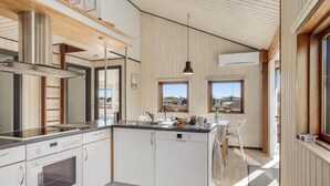 Eine moderne Küche mit weißen Schränken, einer Edelstahl-Dunstabzugshaube und einem Geschirrspüler von Bosch. Zwei Fenster sorgen für natürliches Licht und bieten einen Ausblick ins Freie.