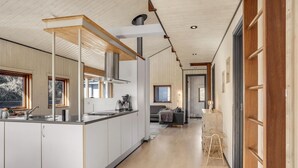 Eine moderne Küche mit einer zentralen Kochinsel, Holzbalkendecke und Blick auf den Wohnbereich.