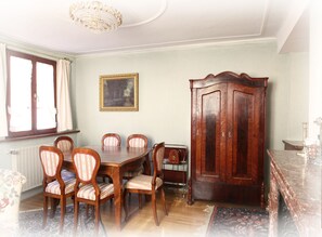 A dining area with a wooden table and chairs, a large wooden cabinet, and a chandelier.