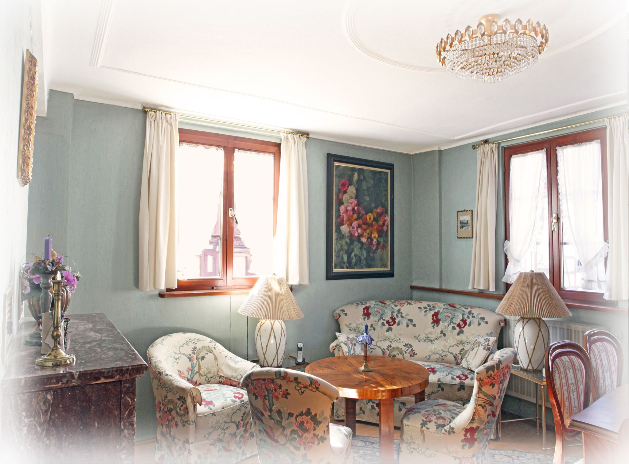 A room with a wooden coffee table, floral armchairs, a sofa, and a chandelier.