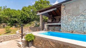Une piscine avec des murs en pierre et un espace barbecue.